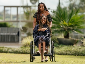 A smiling woman in a wheelchair outside on the grass.