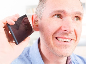 A man with a hearing aid listening to his phone.