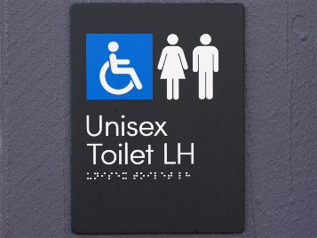 A sign with the disability symbol and unisex symbol. It has Unisex Toilet LH printed on it and braille underneath.