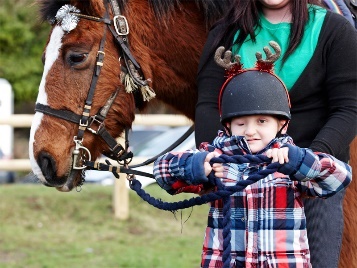A child with a horse. The child is wearing a helmet and holding the reins.